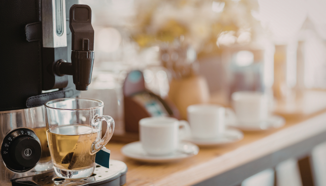 Tea brewing into a glass cup beside other cups, representing a shared morning tea at work.