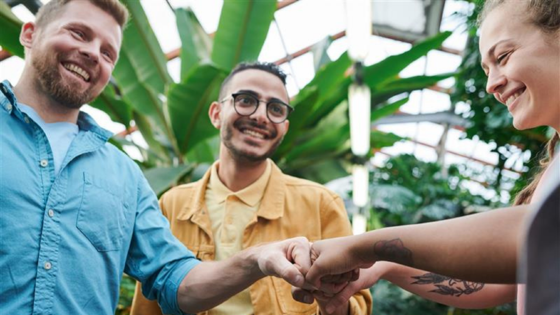 Group of adults smiling as they join fists together, showing teamwork, unity, and shared purpose.