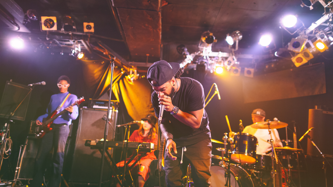 Live band performing on stage under bright lights at an indoor concert venue.