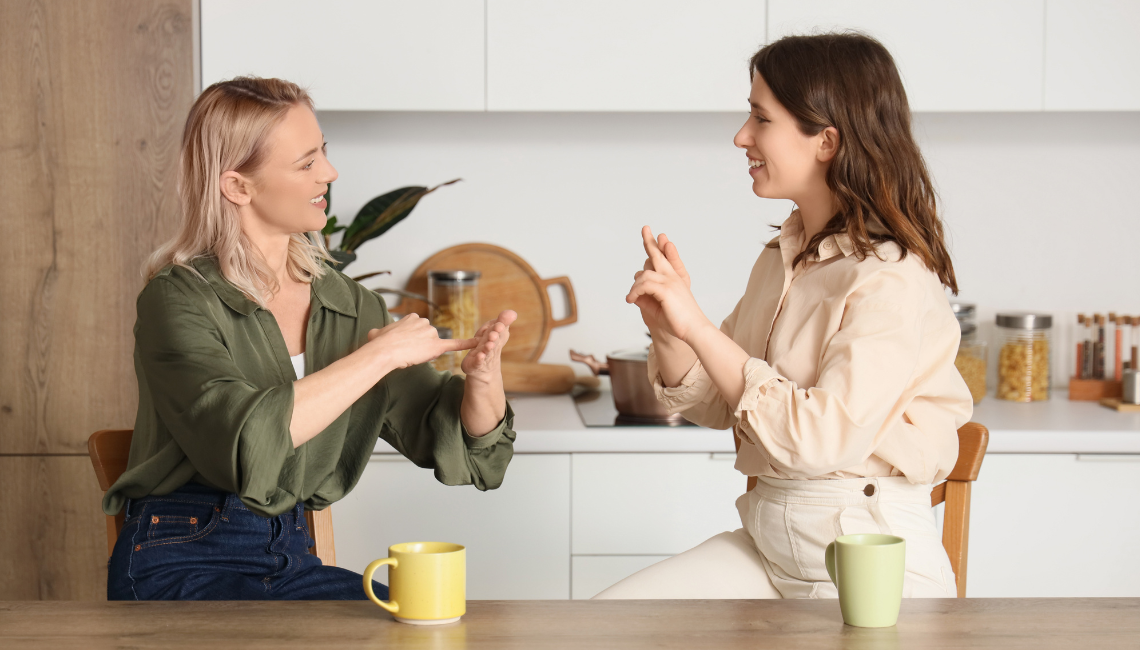 Two ladies using sign language around a table with cups of coffee