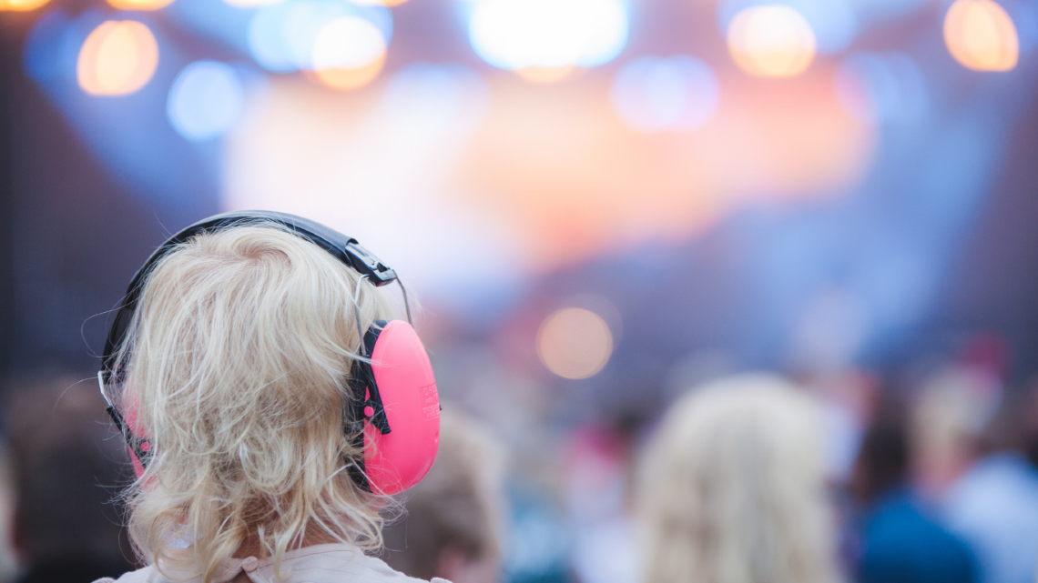 Child wearing pink earmuffs at a loud outdoor event.