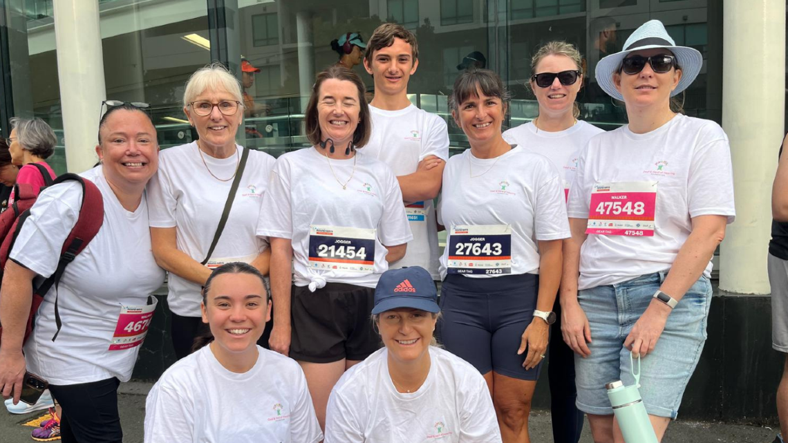 Team of fundraisers in event shirts pose together wearing race bibs before a community run.