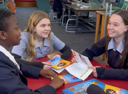 3 Year 9 girls sitting around a table with the Make Listening Safe brochure
