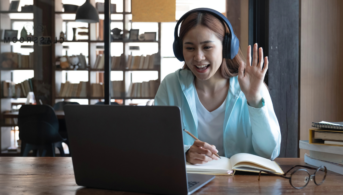 Woman wearing headphone in front of a laptop and having her left hand raised