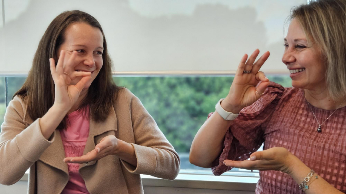 Two women smiling and using sign language during a workplace session.