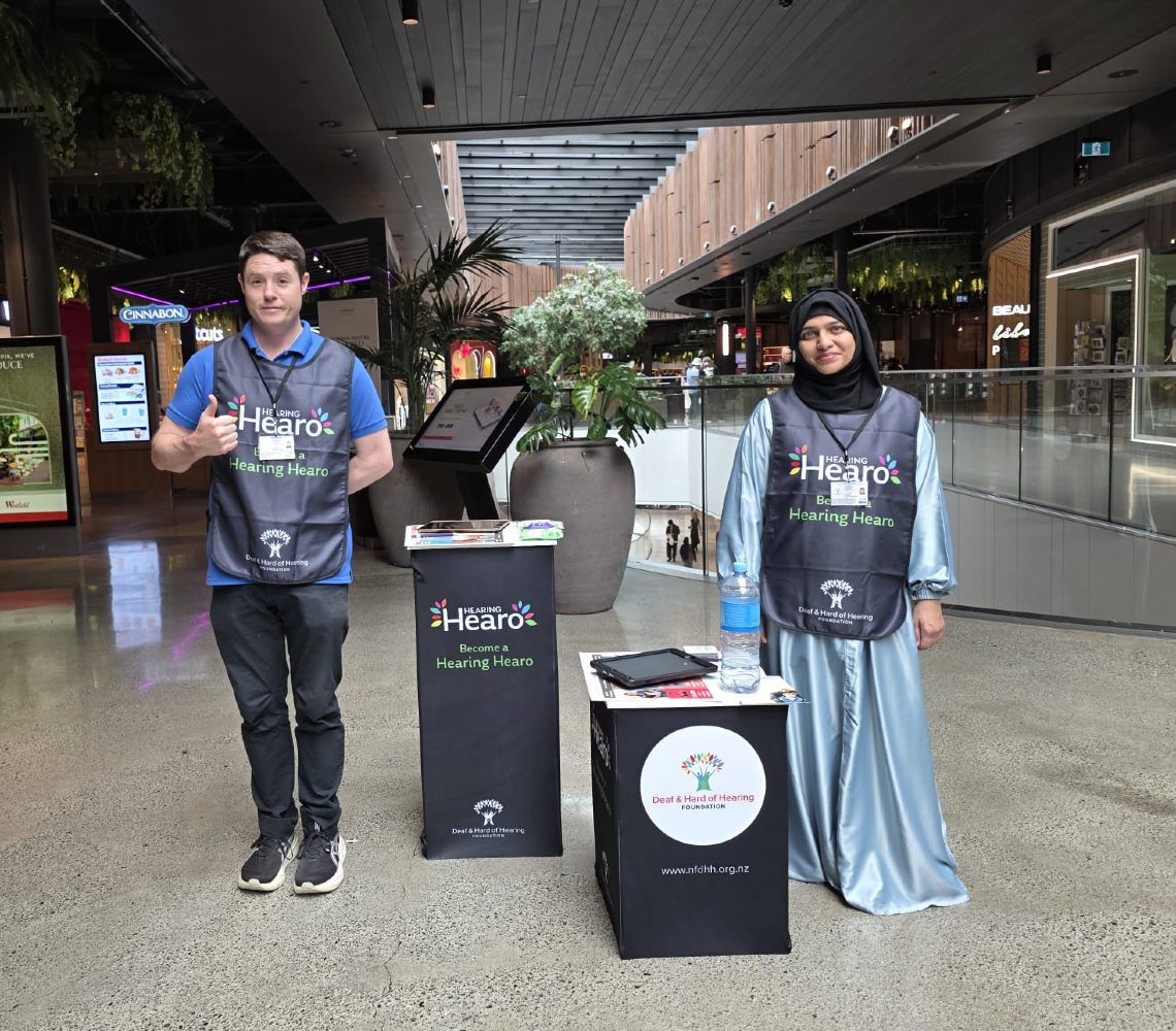 Two Face-to-Face fundraisers at a Hearing Hearo information stand in a shopping centre, inviting people to support the Deaf & Hard of Hearing Foundation.