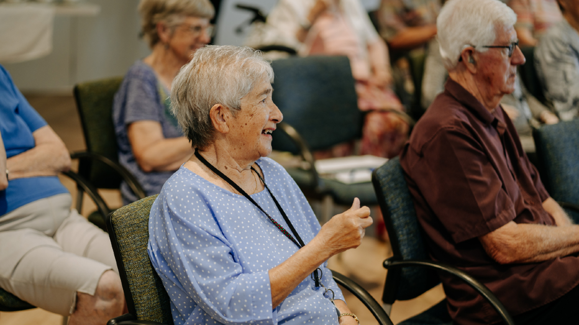 Older adults seated and smiling during a community event.