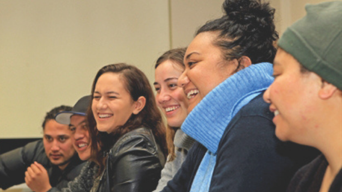 Group of young adults laughing together in a classroom, showing connection and shared learning.