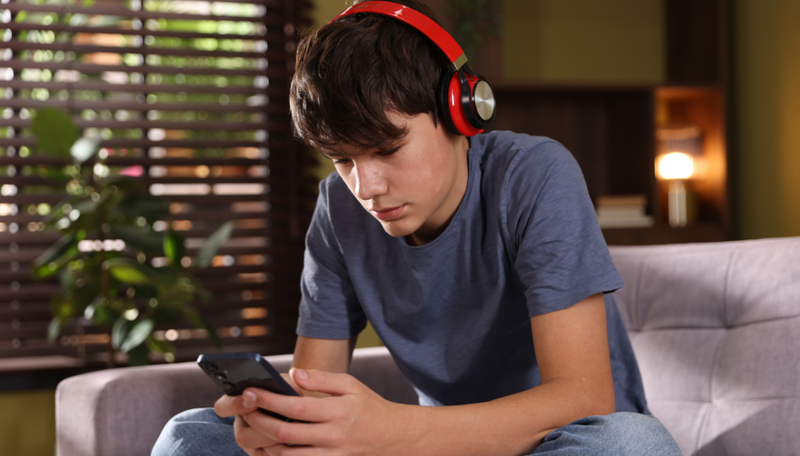 Teenager wearing headphones and looking at a phone during a school hearing screening.