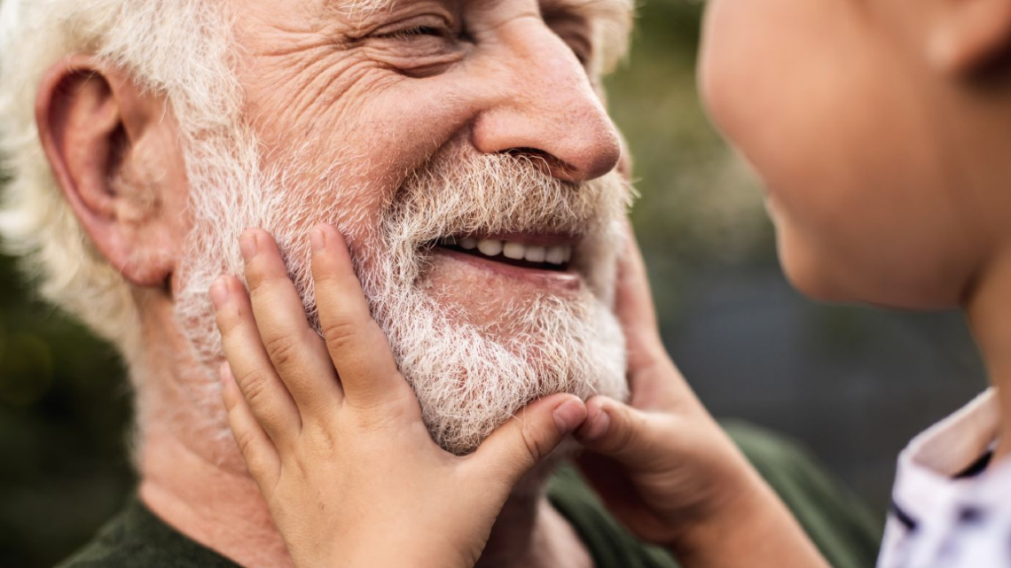 Older man smiling as a child gently holds his face, showing love, closeness, and family connection.