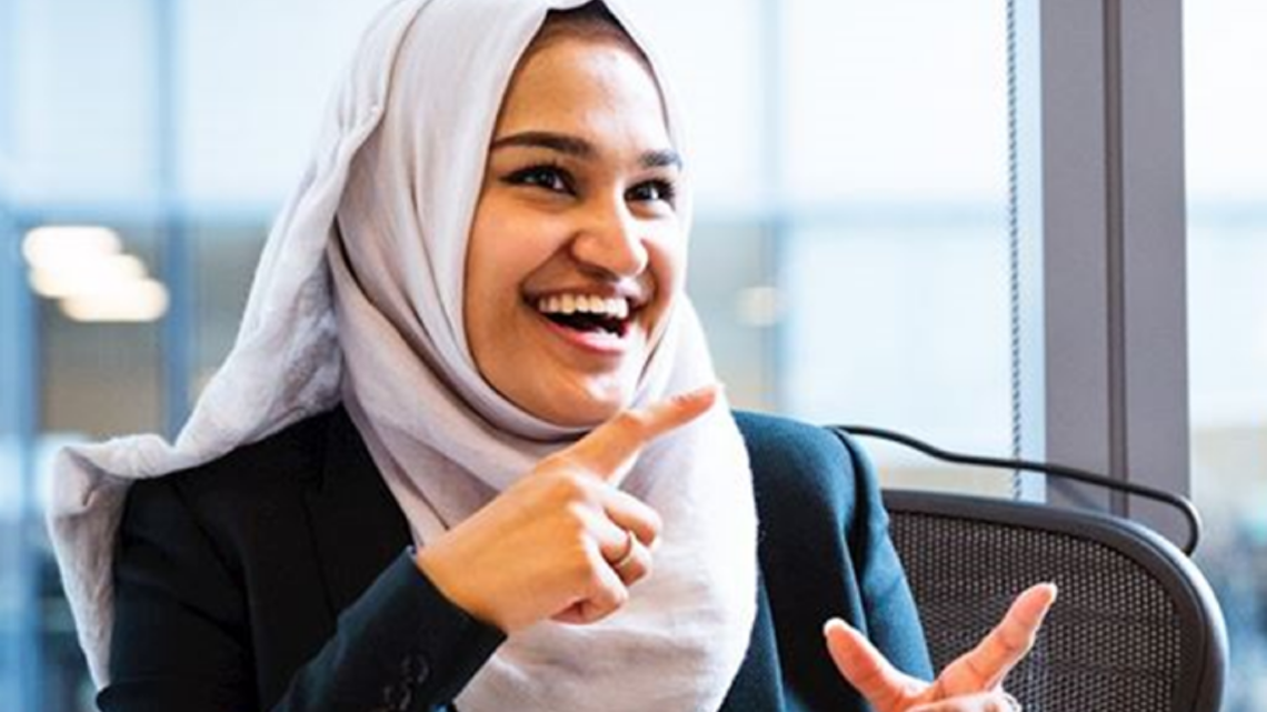 Smiling woman in a hijab gesturing during a workplace conversation.