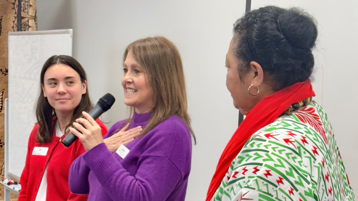 Three women speaking at a community event, with one holding a microphone.