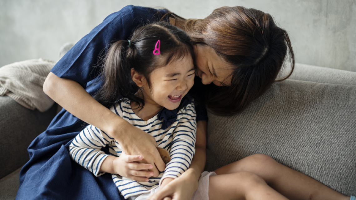 Mother cuddling a laughing young child on a sofa at home.