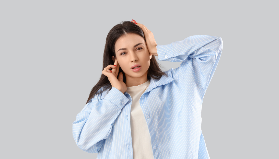 Woman holding her ear and head, representing tinnitus symptoms or ear pain.