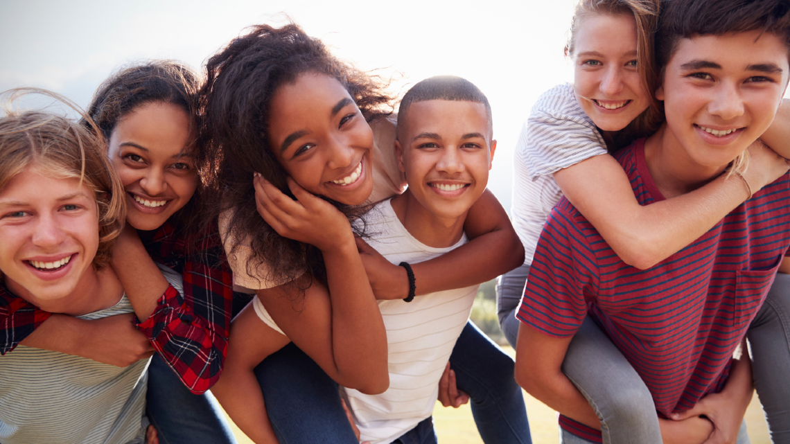 Group of teenagers smiling together outdoors, showing friendship, connection, and shared support.