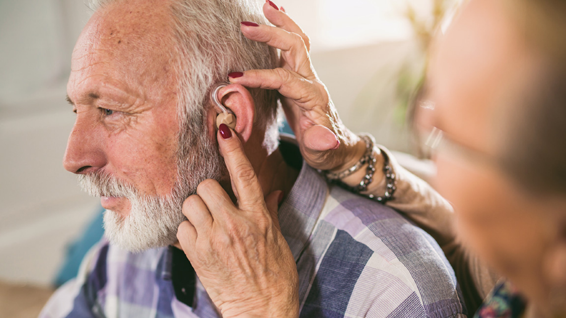 Older man having a hearing aid adjusted, showing access to hearing support and care.