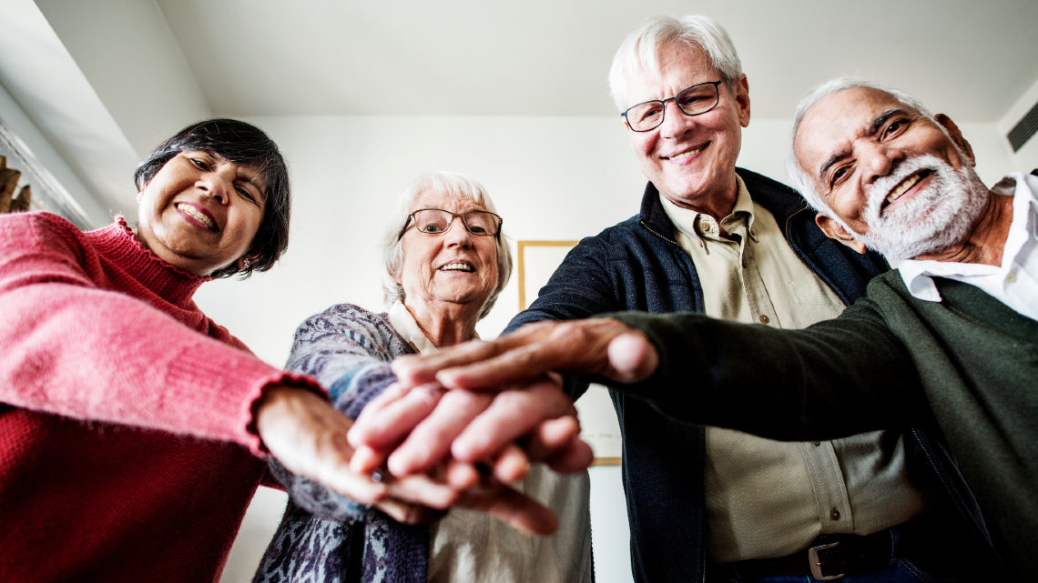 Older adults standing together with hands stacked, showing teamwork, support, and community.