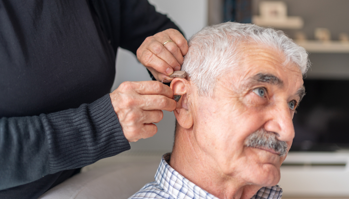 Older man with white hair being fitted with a hearing aid