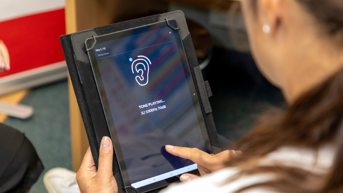 Student uses a tablet displaying hearing test tones during a school screening.