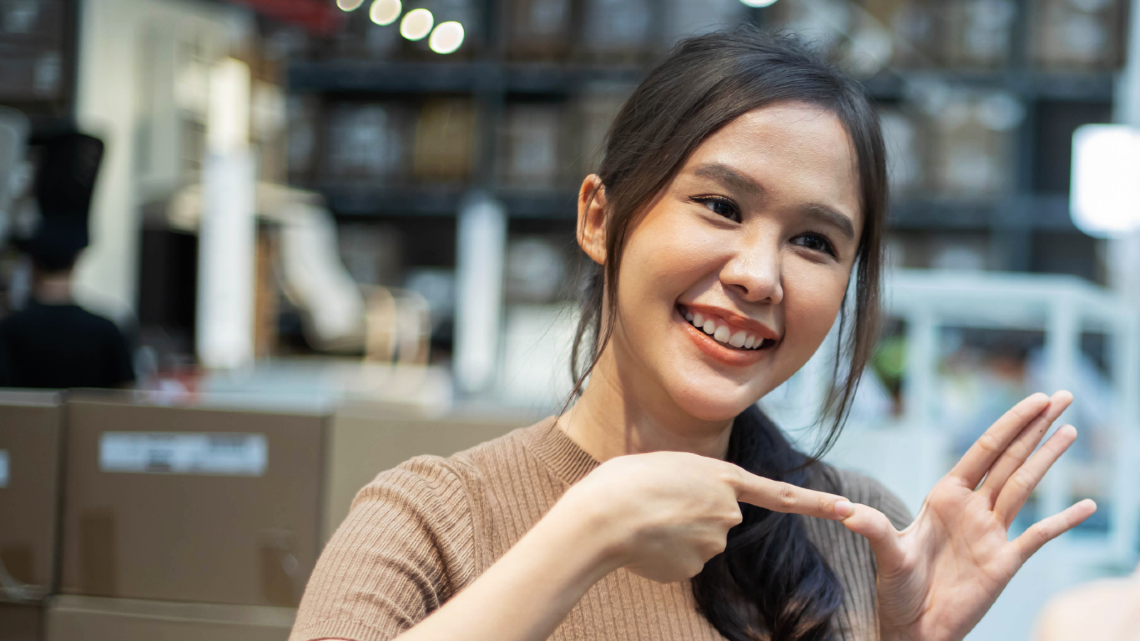 Woman signs while smiling to another person in a workplace, suggesting a friendly conversation in sign language.