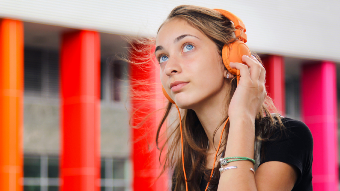 Female teenager with blond hair and blue eyes, wearing orange headphones.