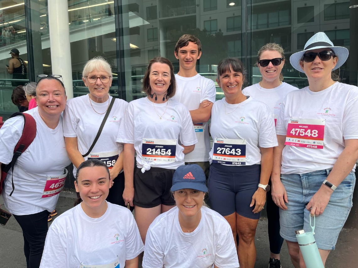 Team of fundraisers in event shirts pose together wearing race bibs before a community run.