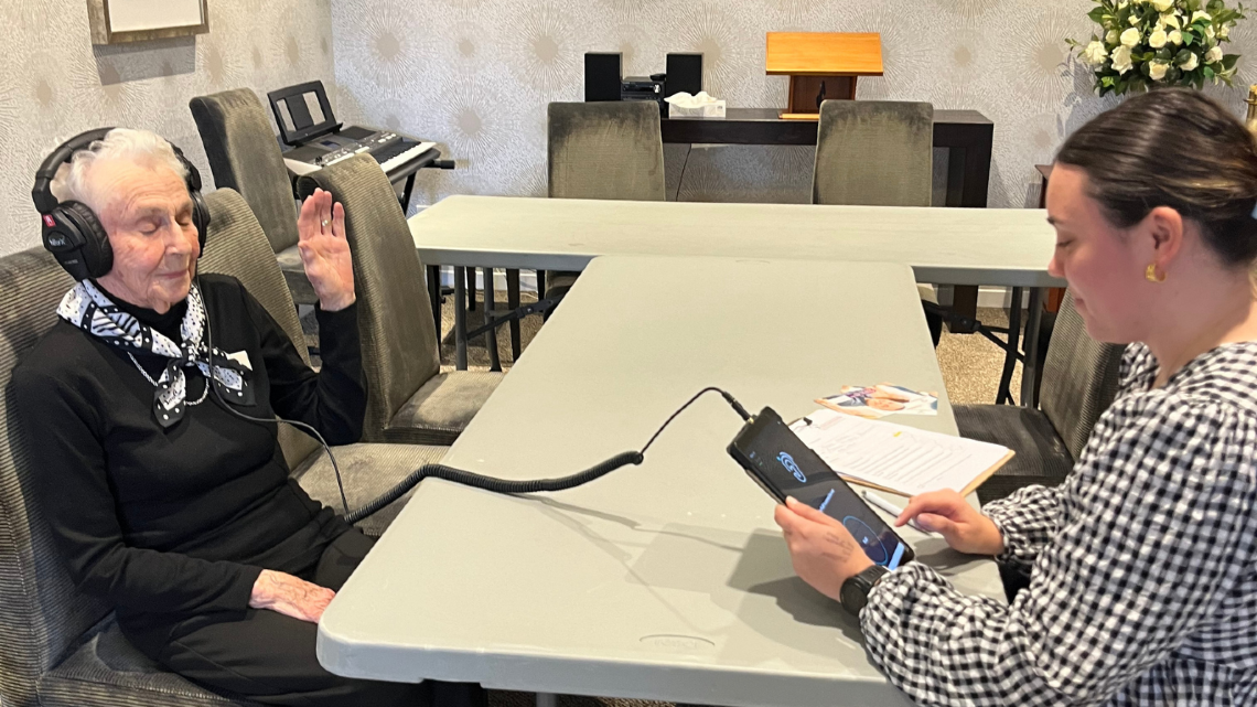 Older woman wearing headphones during a hearing check with a staff member.