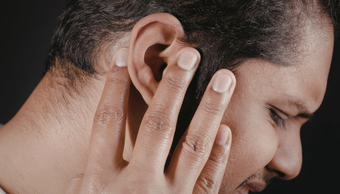 Man pressing his ear in discomfort, representing tinnitus or ongoing ear-related symptoms.