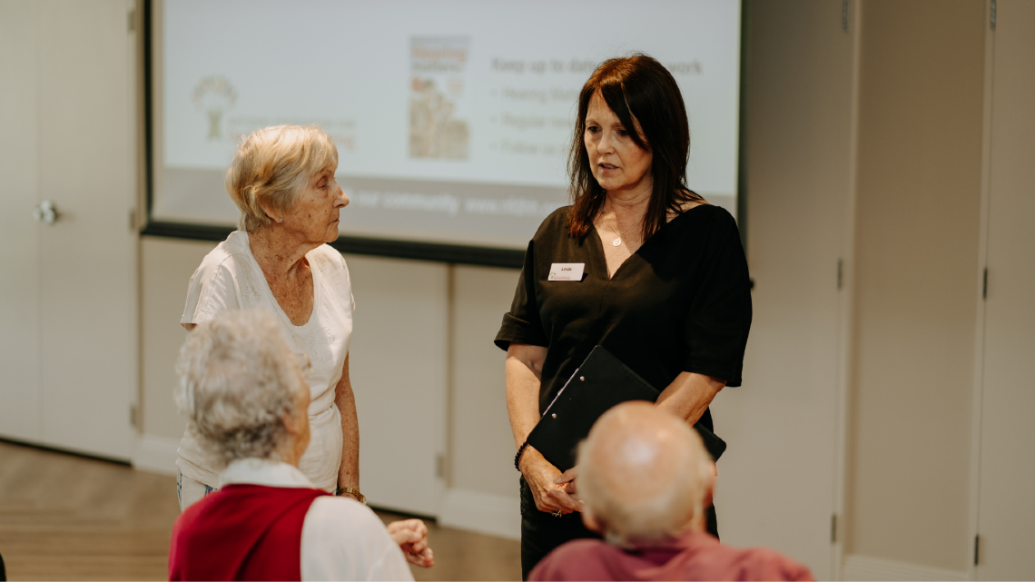 Staff member speaking with older residents during a retirement village outreach session.