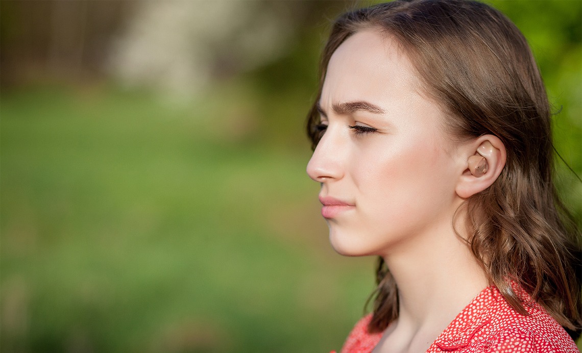Woman and young boy touch foreheads outdoors, with the boy wearing a cochlear implant sound processor.