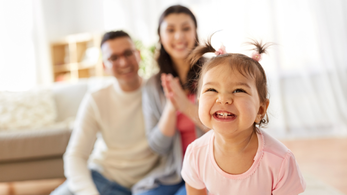 Smiling young child in the foreground with parents behind, showing family joy, connection, and everyday support.