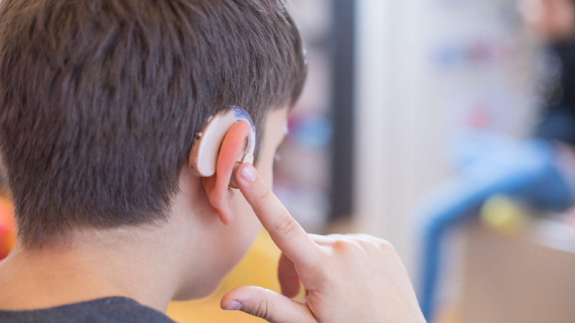 Child touching a cochlear implant behind their ear in a close-up side view.