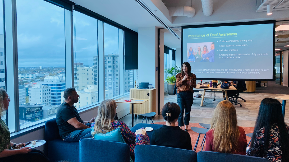 Presenter speaking to a group during a Deaf awareness session in an office.