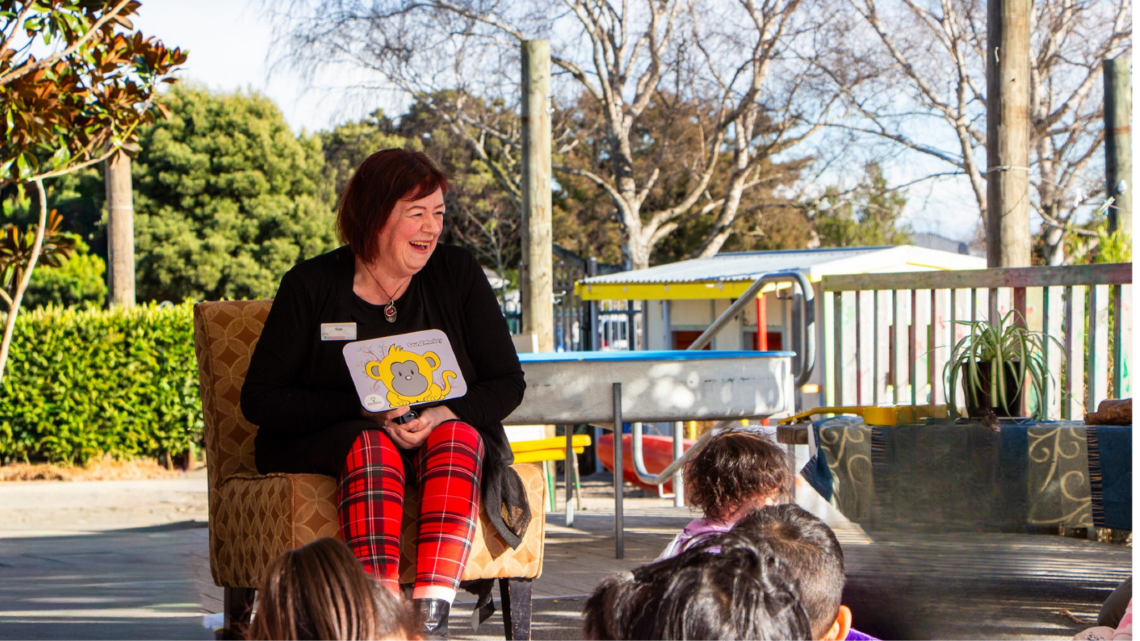 Community Partnership Administrator holding a Sound Monkey board book while reading to young children outdoors.