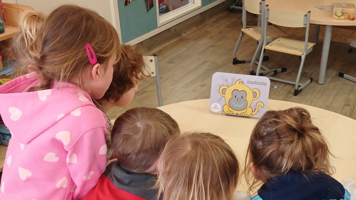 Young children gathered around a table watching Sound Monkey in action.