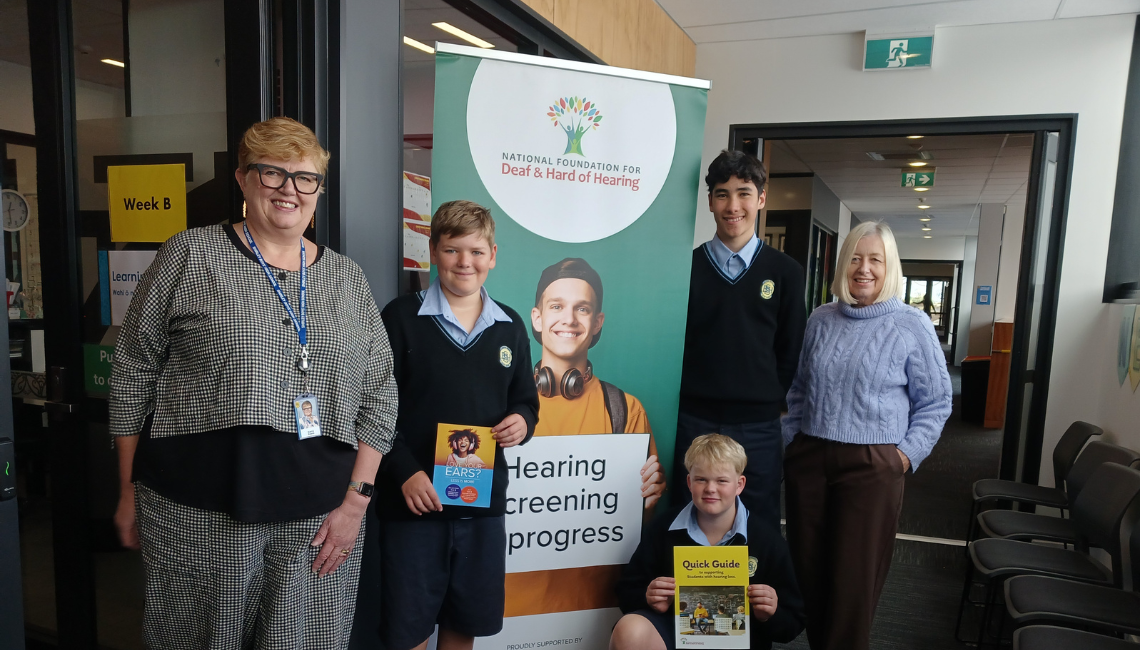 Students and staff stand beside a National Foundation for Deaf & Hard of Hearing banner promoting hearing screening at school.