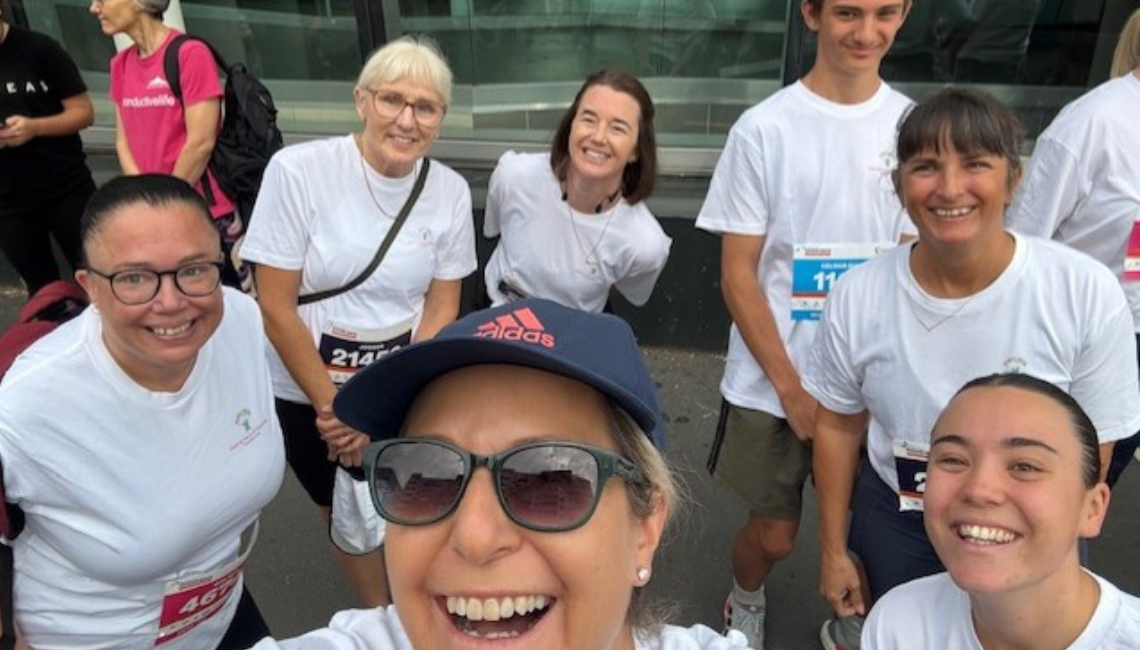 Team of fundraisers in event shirts pose together wearing race bibs before a community run.