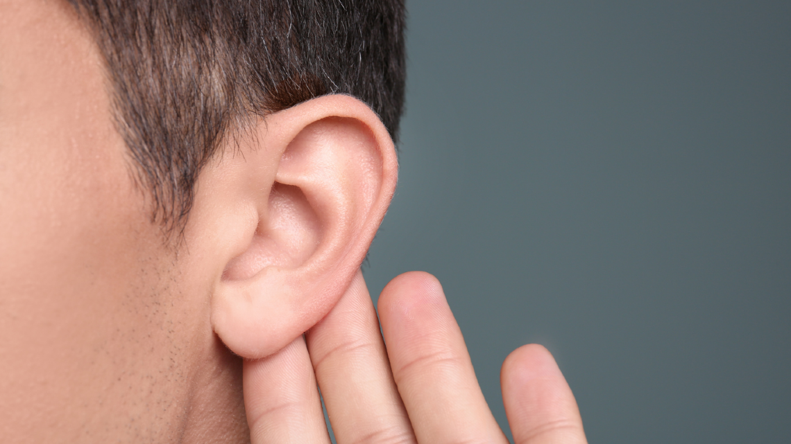 Close-up of an ear with a hand cupped behind it, representing listening and hearing awareness.