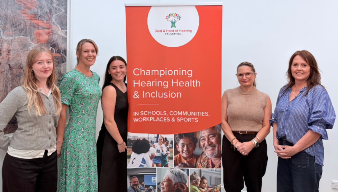 Five staff members standing beside a Deaf and Hard of Hearing Foundation banner.