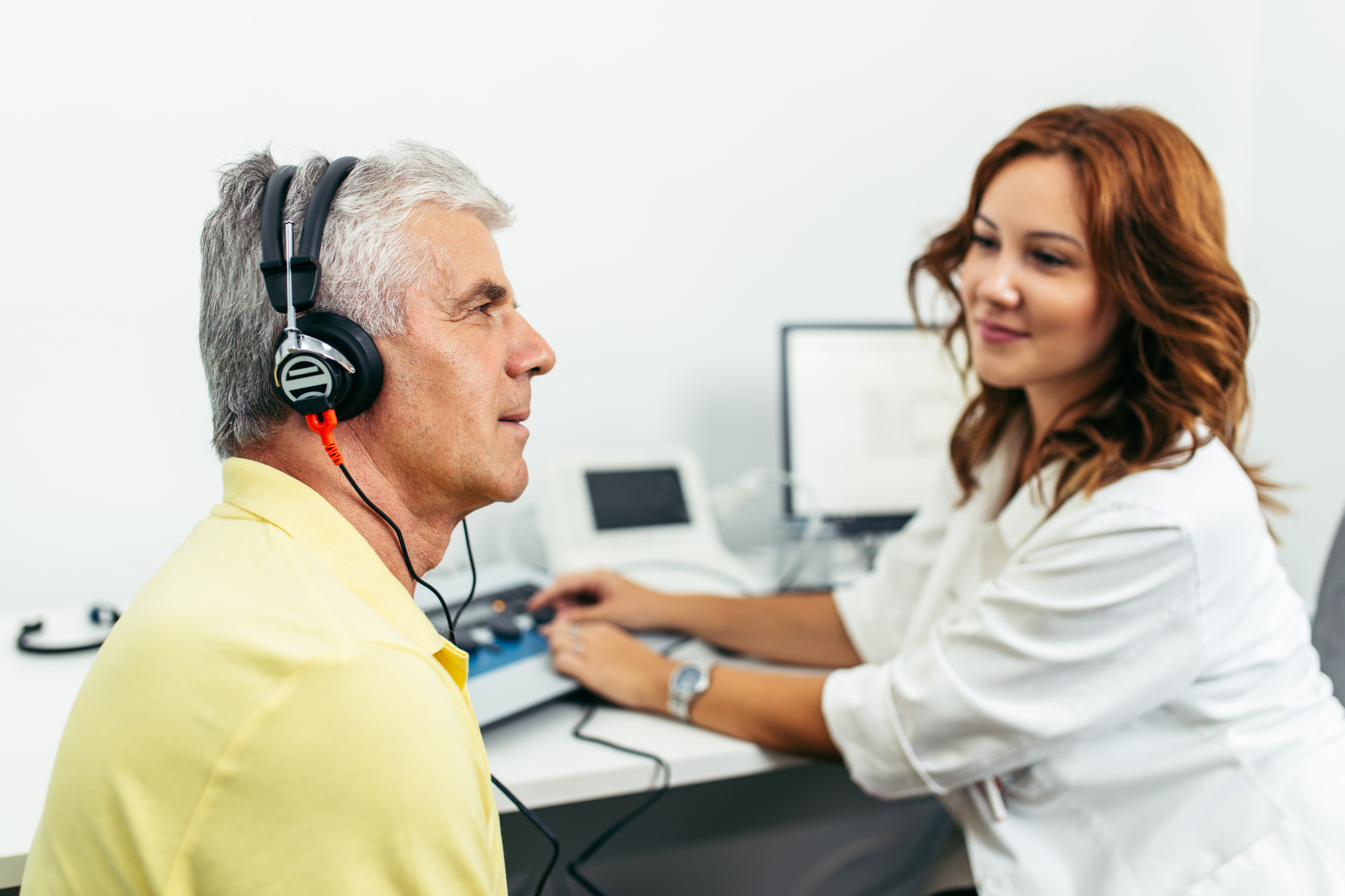 An older man wears headphones during a hearing screening while a clinician operates the testing equipment.