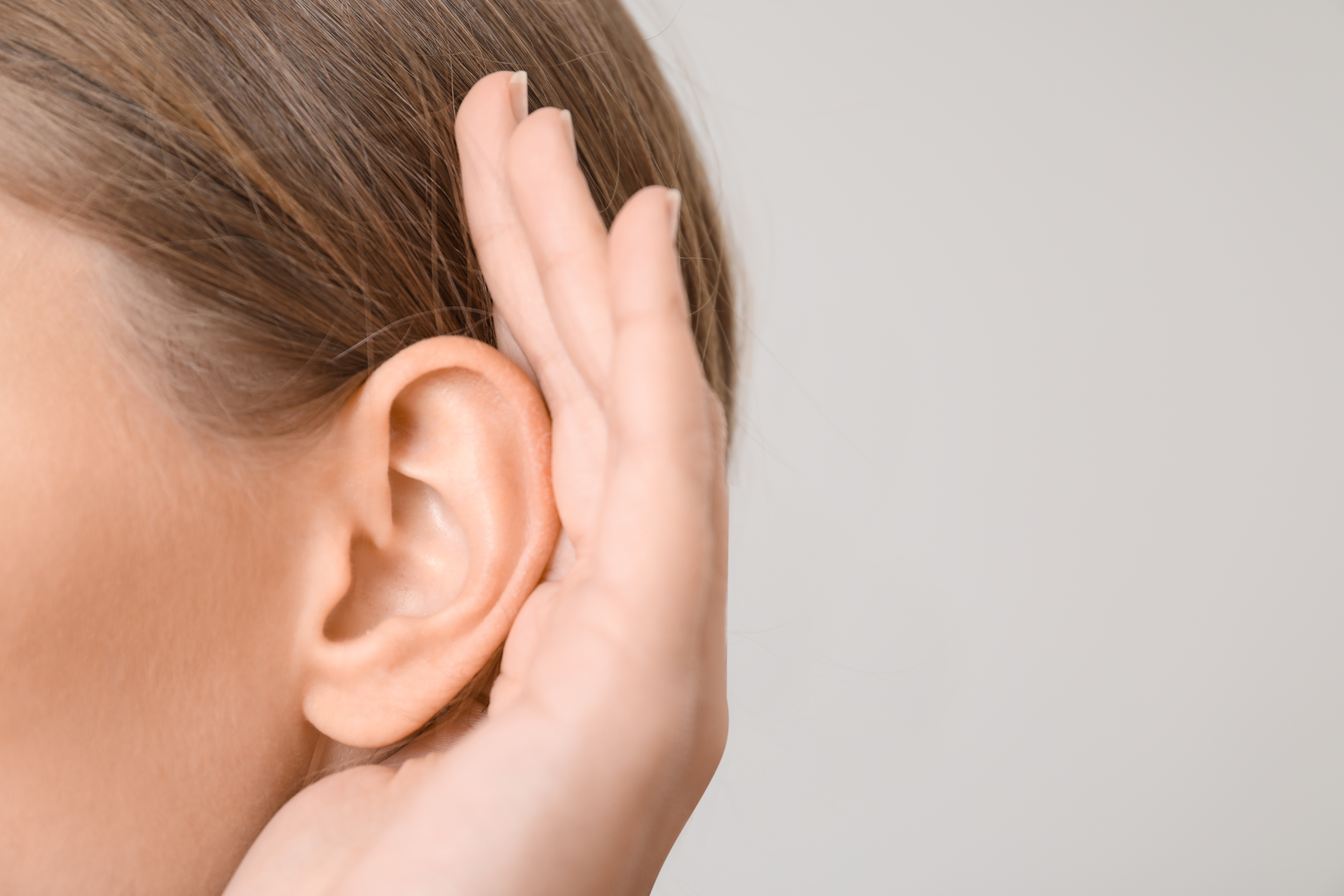 Close-up of an ear with a hand cupped behind it, representing hearing loss and listening difficulty.