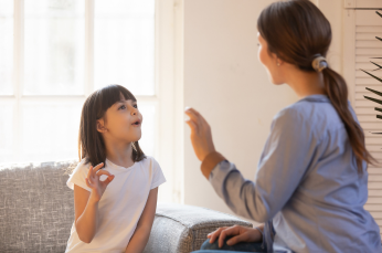 A mom and daughter learning sign language in their lounge