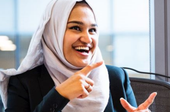 Woman signs while smiling in an office, representing support for Deaf customers through accessible communication.