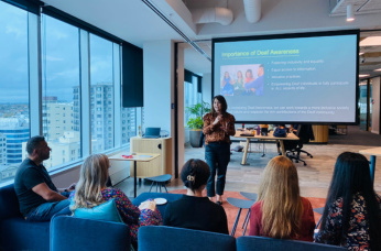 Presenter gives a deaf awareness session to workplace staff in a meeting room with a presentation screen.