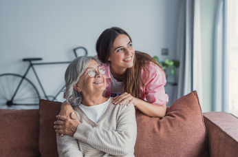 Mother and daughter share a happy moment on a sofa, representing hearing intervention and the importance of family connection.