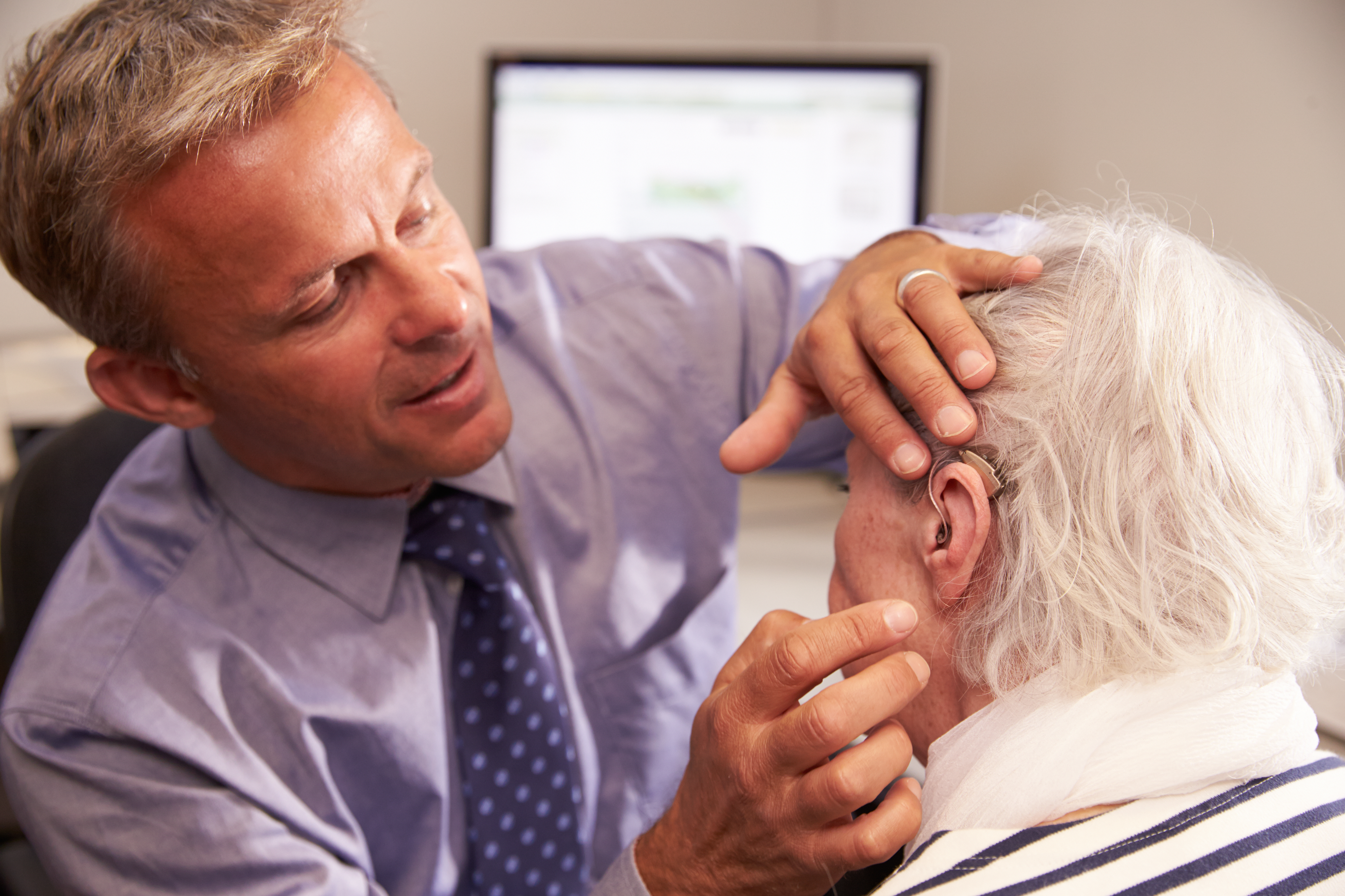 Audiologist checks an older woman&rsquo;s hearing aid during an appointment.