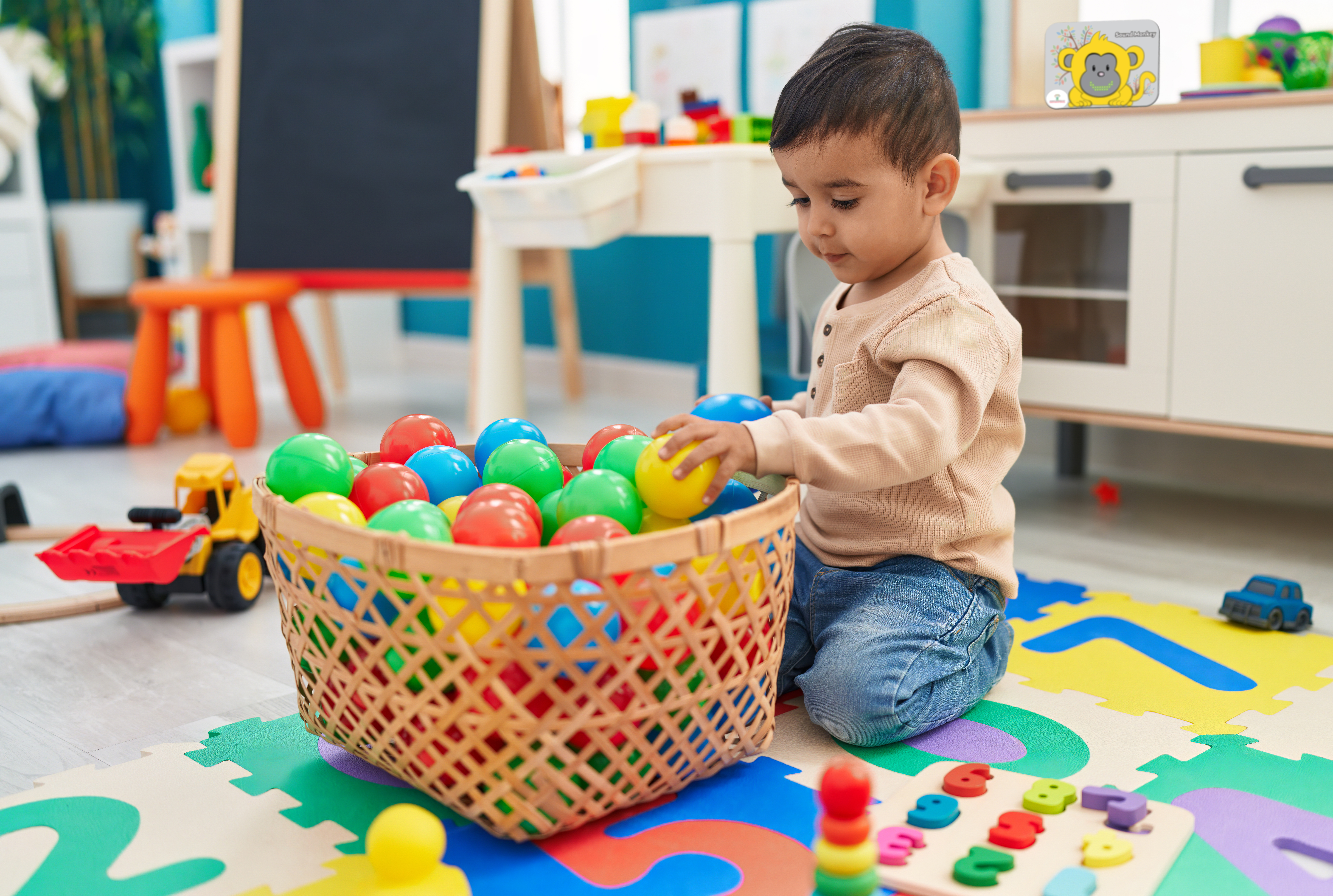 Toddler playing with plastic balls with a Sound Monkey in the background