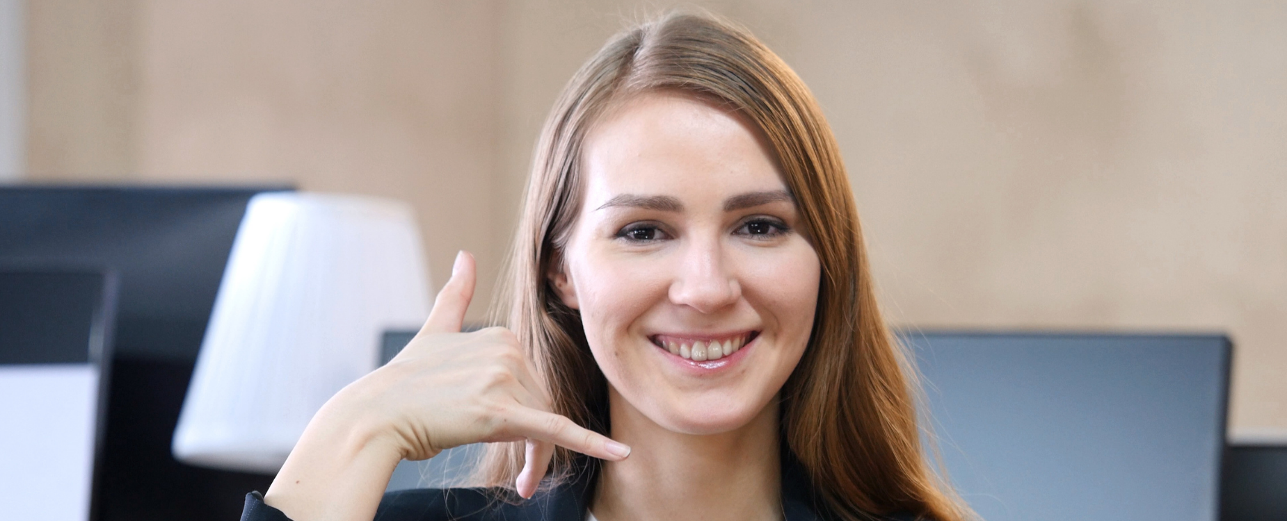 Smiling woman making a phone gesture, representing friendly customer support on the contact us page.