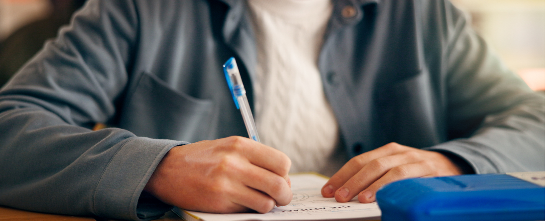 Picture of a person writing in a workbook with a blue pen