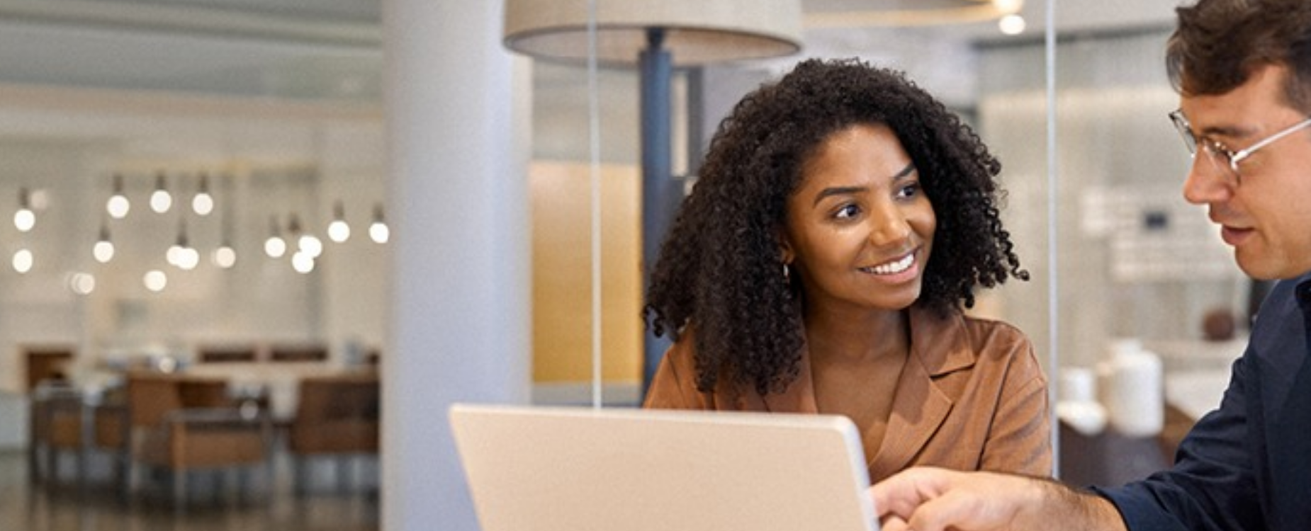 Two colleagues work together at a laptop in an office, representing employers learning more inclusive and accessible workplace practices.